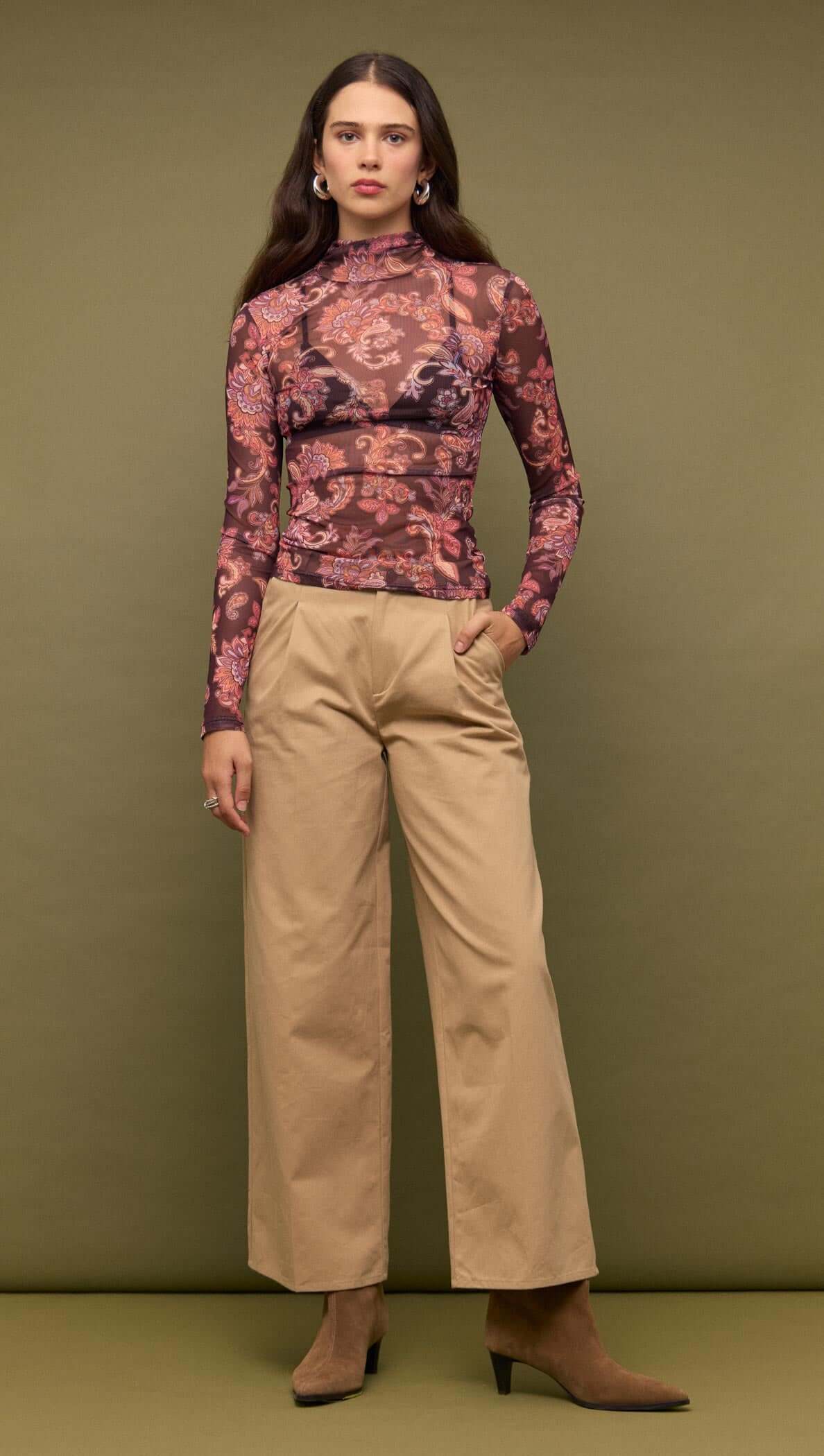 Model wearing a Sheer Printed Long Sleeve Mesh Top with patterned fabric and high neckline, styled with wide-leg pants.