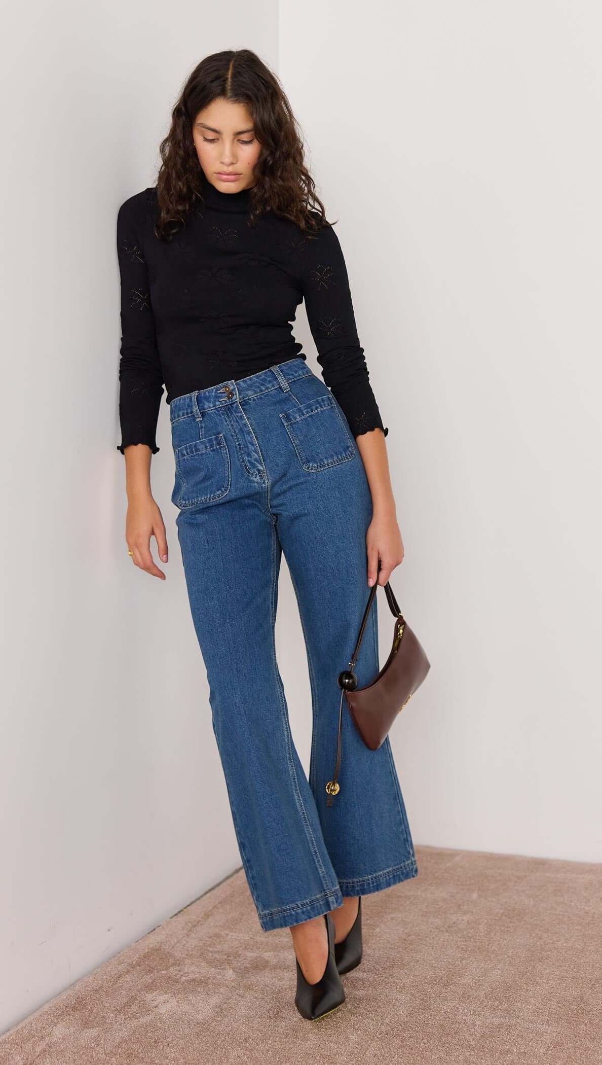 Woman wearing vintage blue high-waisted bootcut jeans with a black top and holding a small handbag.