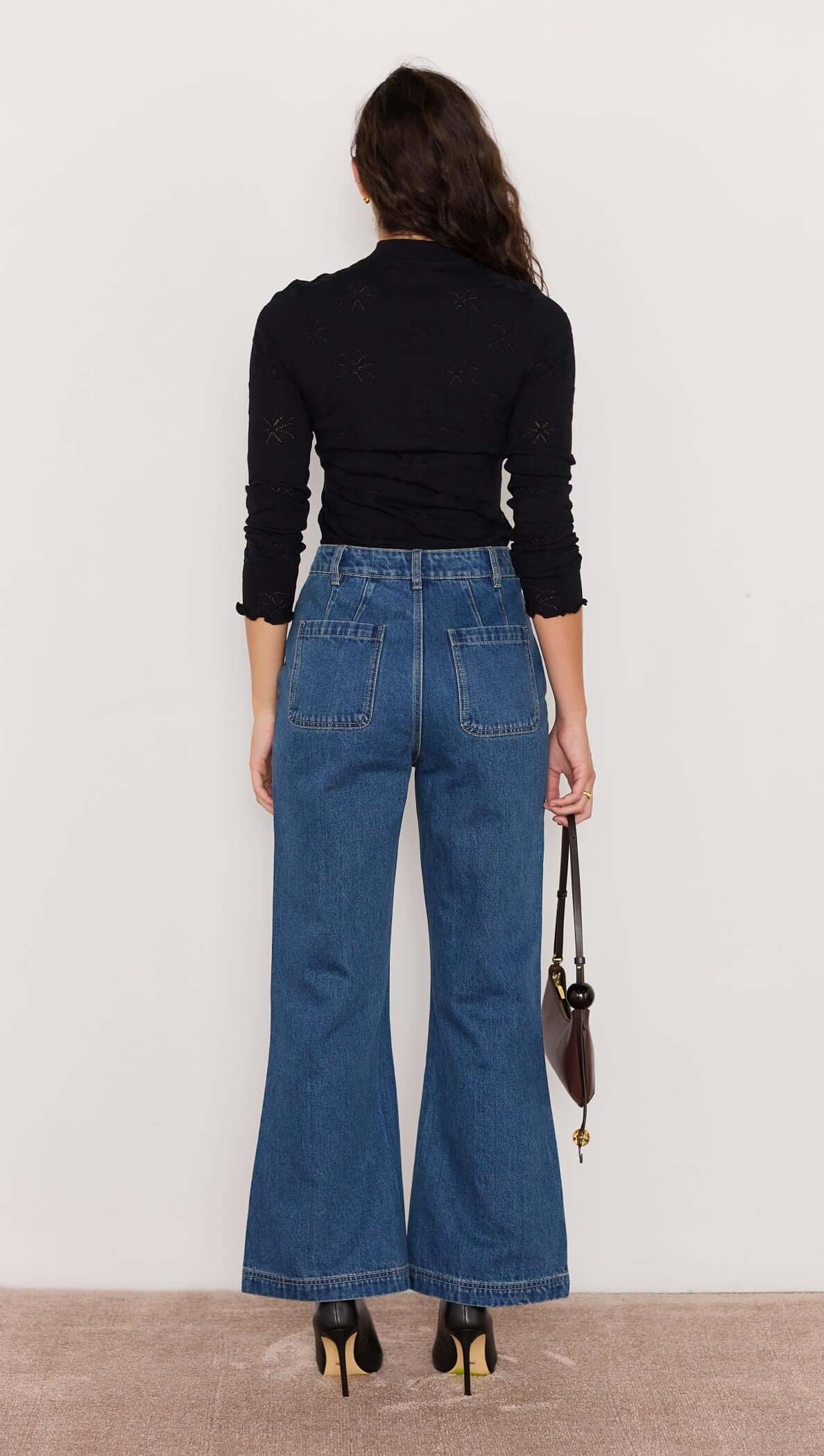 Rear view of a woman wearing Nora Bootcut Jeans with a black top, showcasing a vintage blue wash and flared hem.
