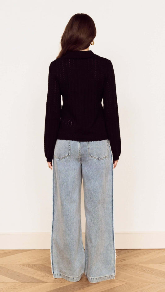 Back view of a woman wearing a Black Scallop Edge Pointelle Cardigan with wide-leg jeans.