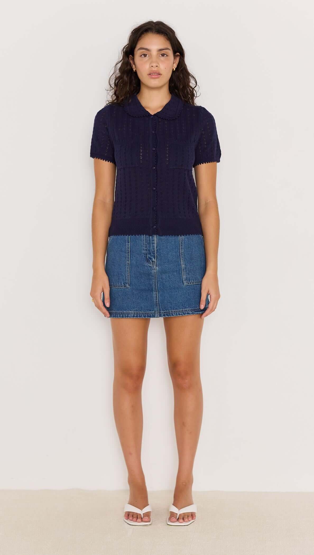 Model wearing a navy pointelle knit tee with a Peter Pan collar, paired with a denim skirt and sandals.