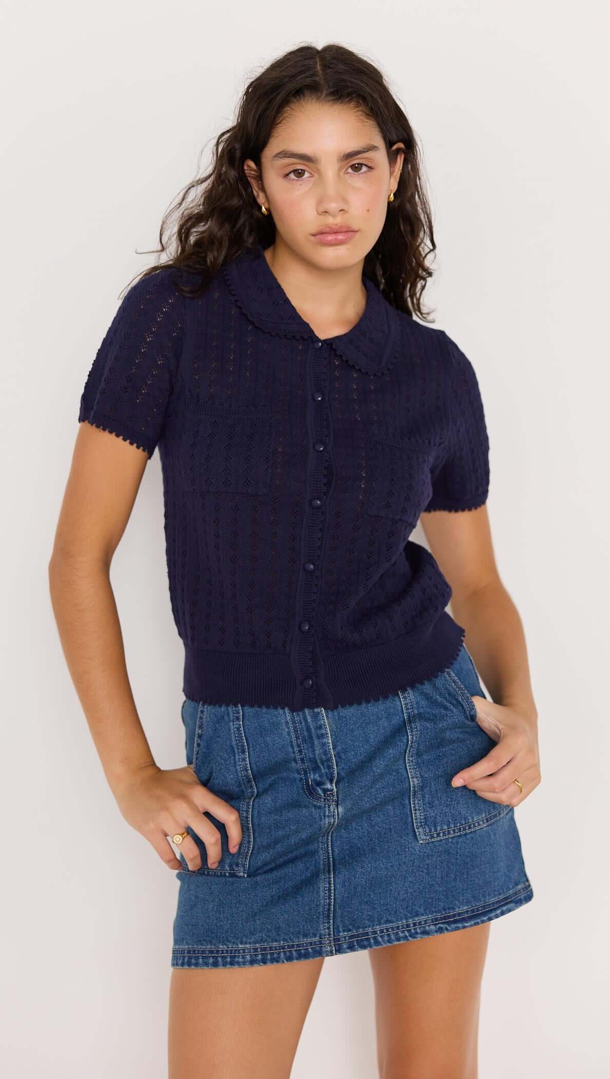Model wearing a vintage-inspired navy pointelle knit tee with a Peter Pan collar and scalloped edges, paired with a denim skirt.