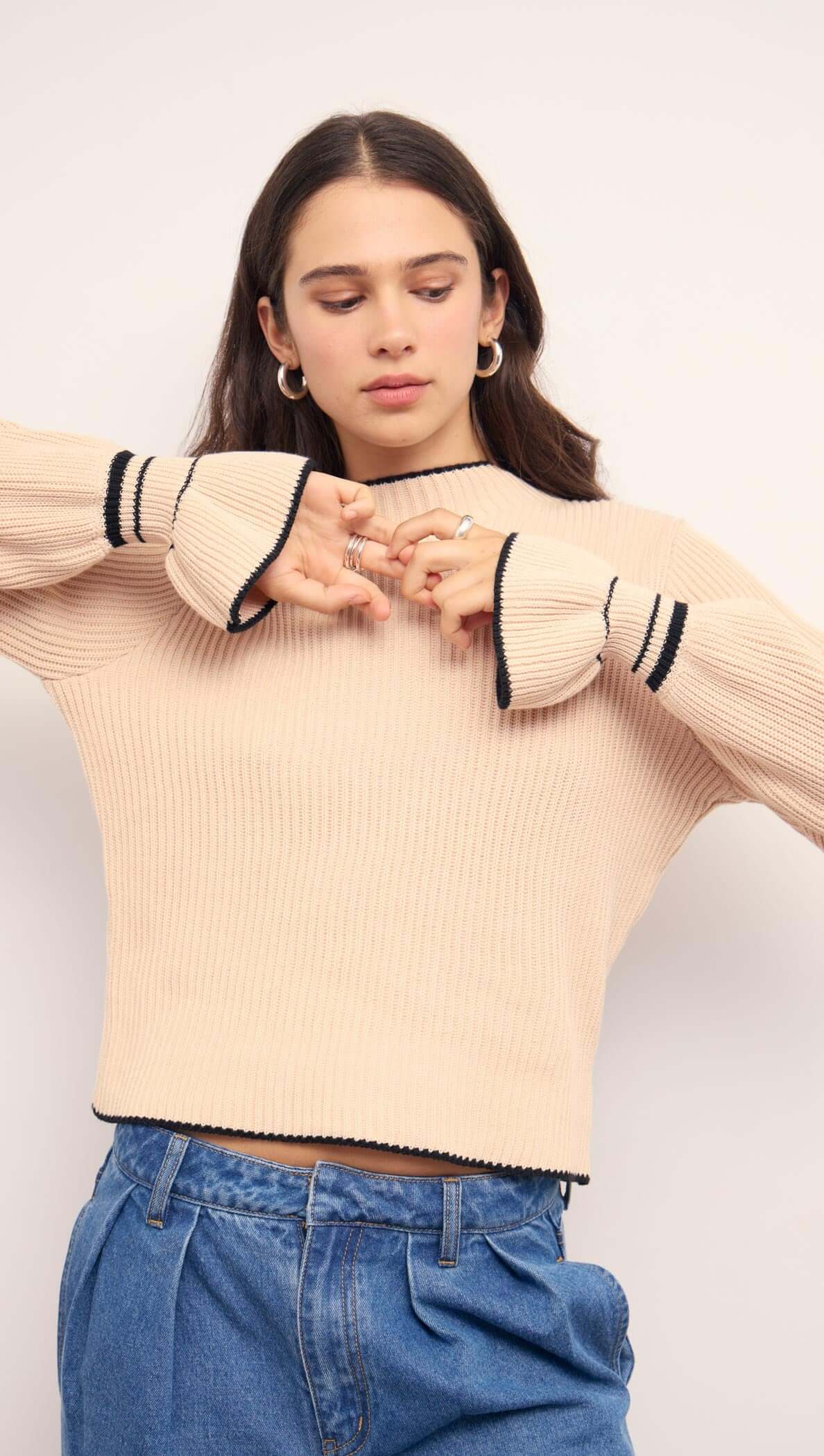 Model wearing Cream Knit Top with Contrast Trim, featuring flared cuffs and a relaxed fit in a ribbed knit design.