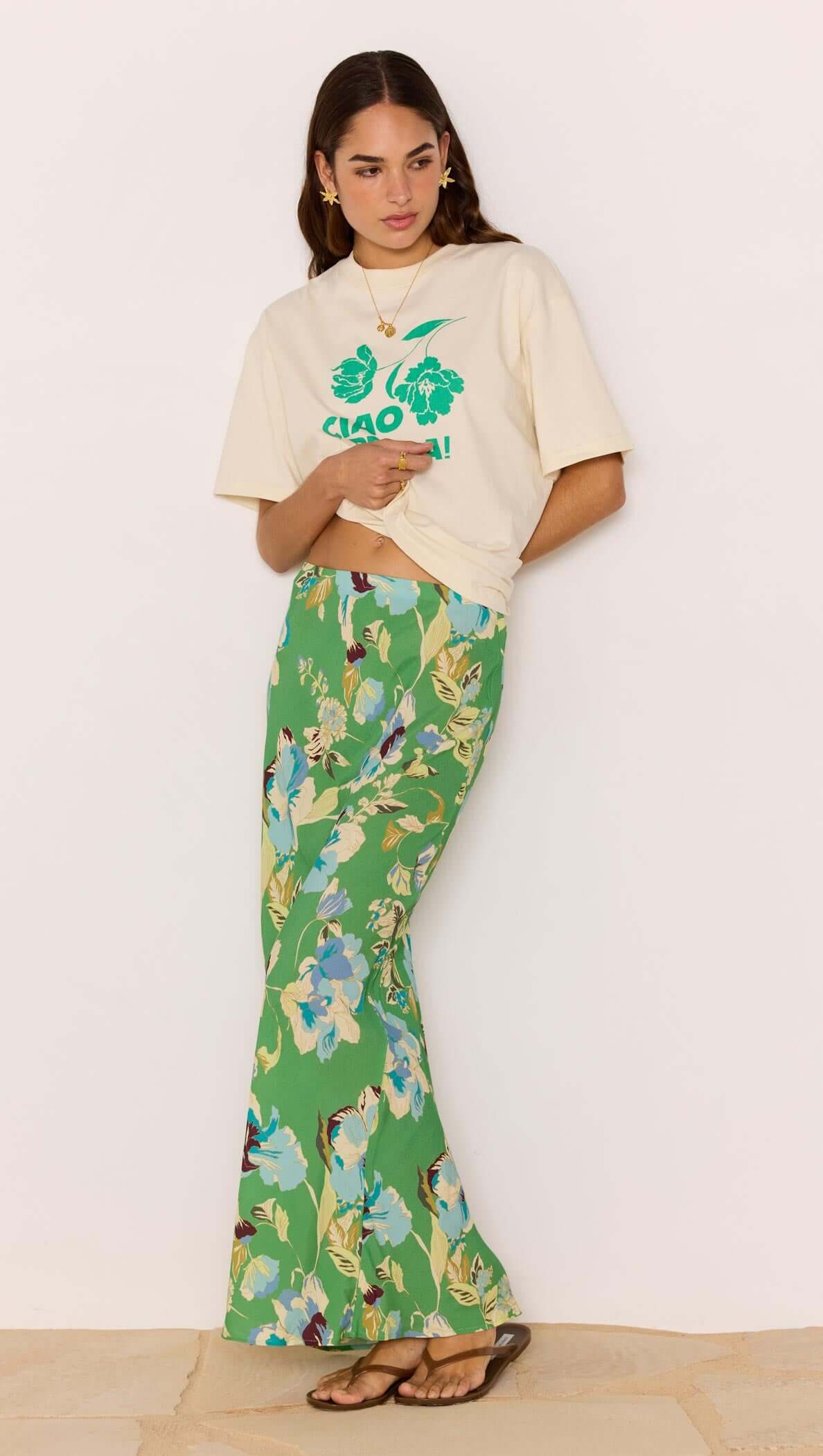 Model wearing a Green Floral Bias Midi Skirt paired with a graphic tee and sandals, showcasing a vibrant floral design.
