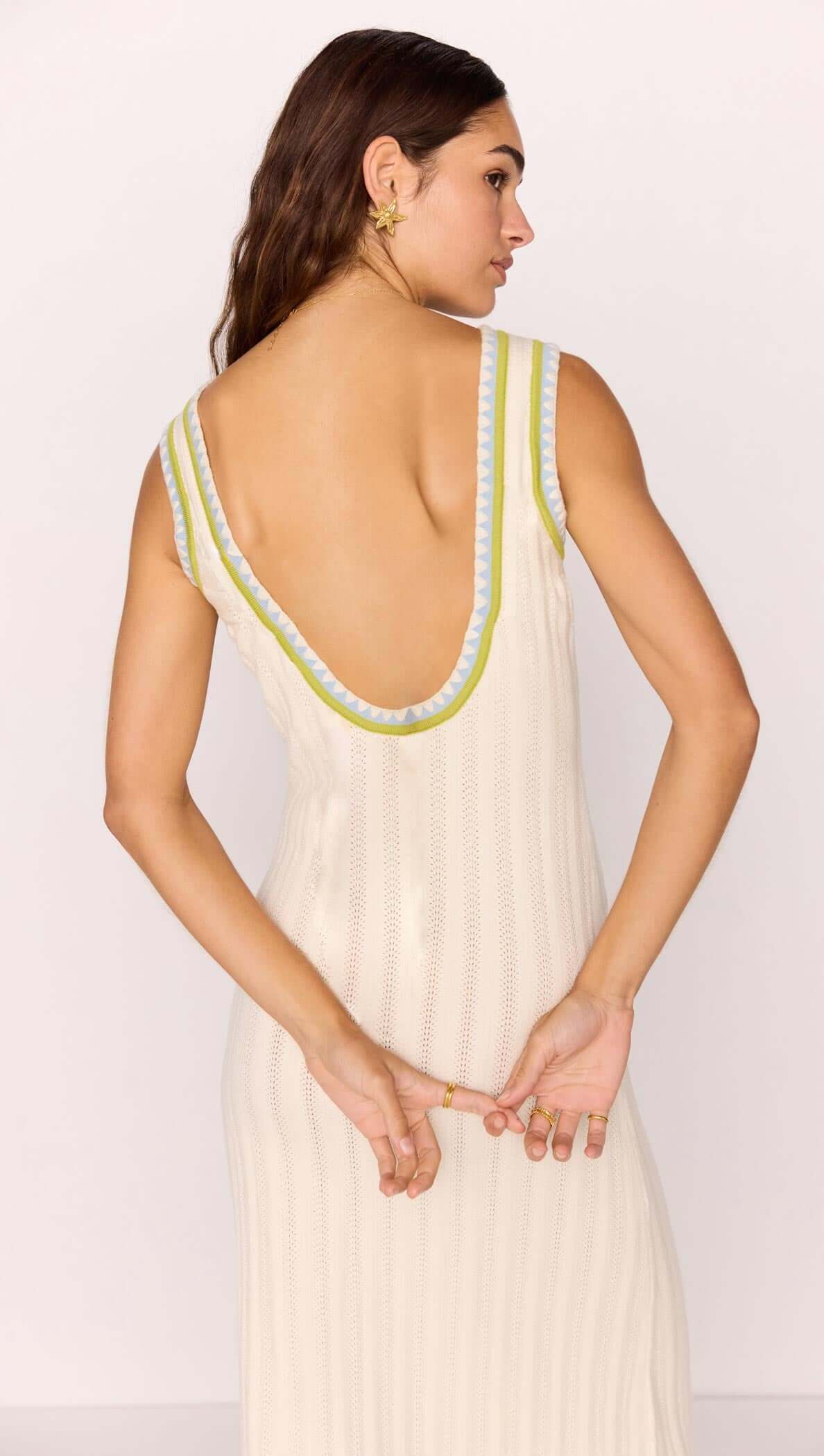 Back view of a woman wearing a white knit midi dress with contrast green trim, showcasing a deep V-neckline.
