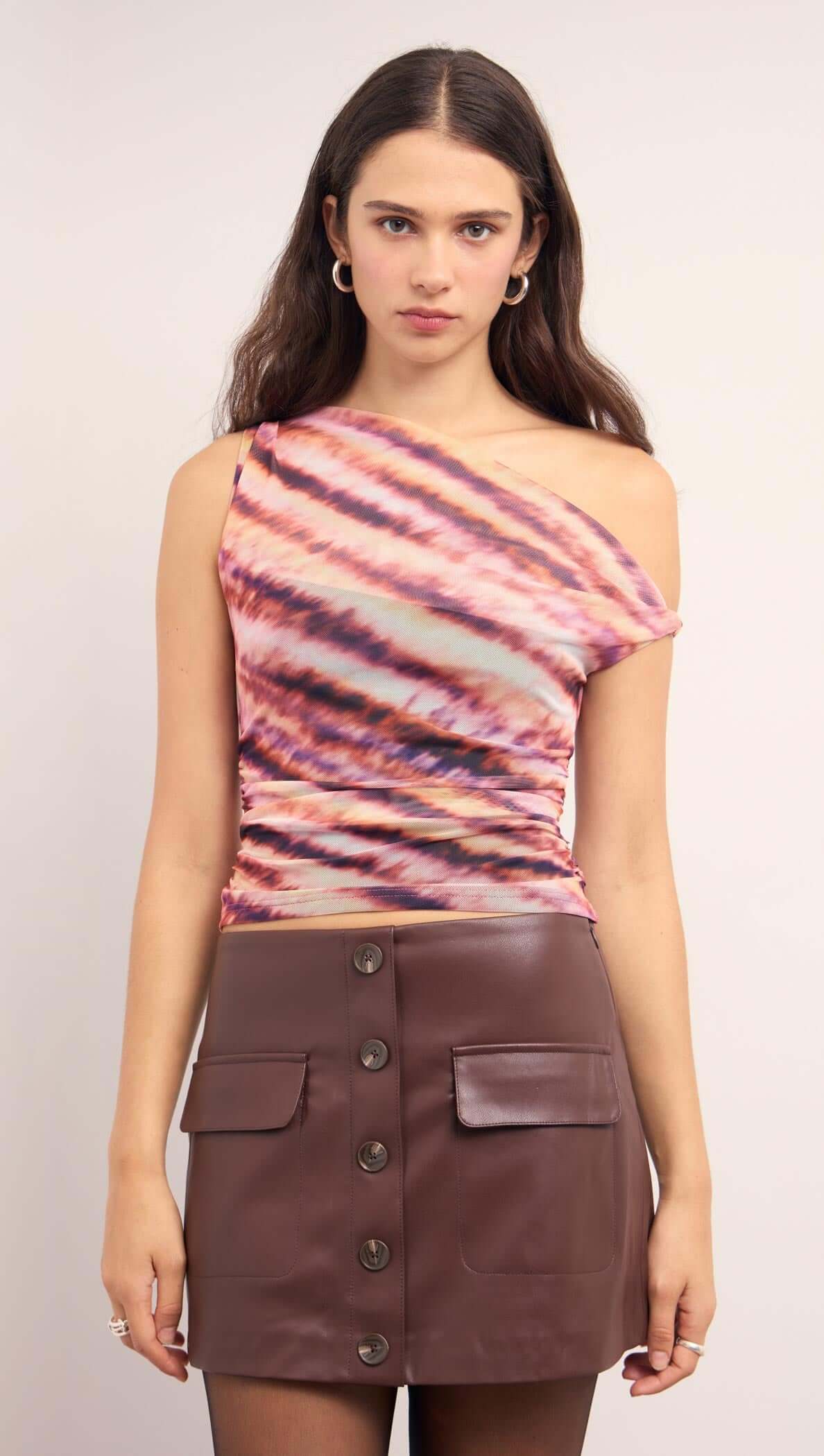 Model wearing a Pink & Purple Striped Mesh Top with asymmetric one-shoulder cut and ruched sides, paired with a brown mini skirt.