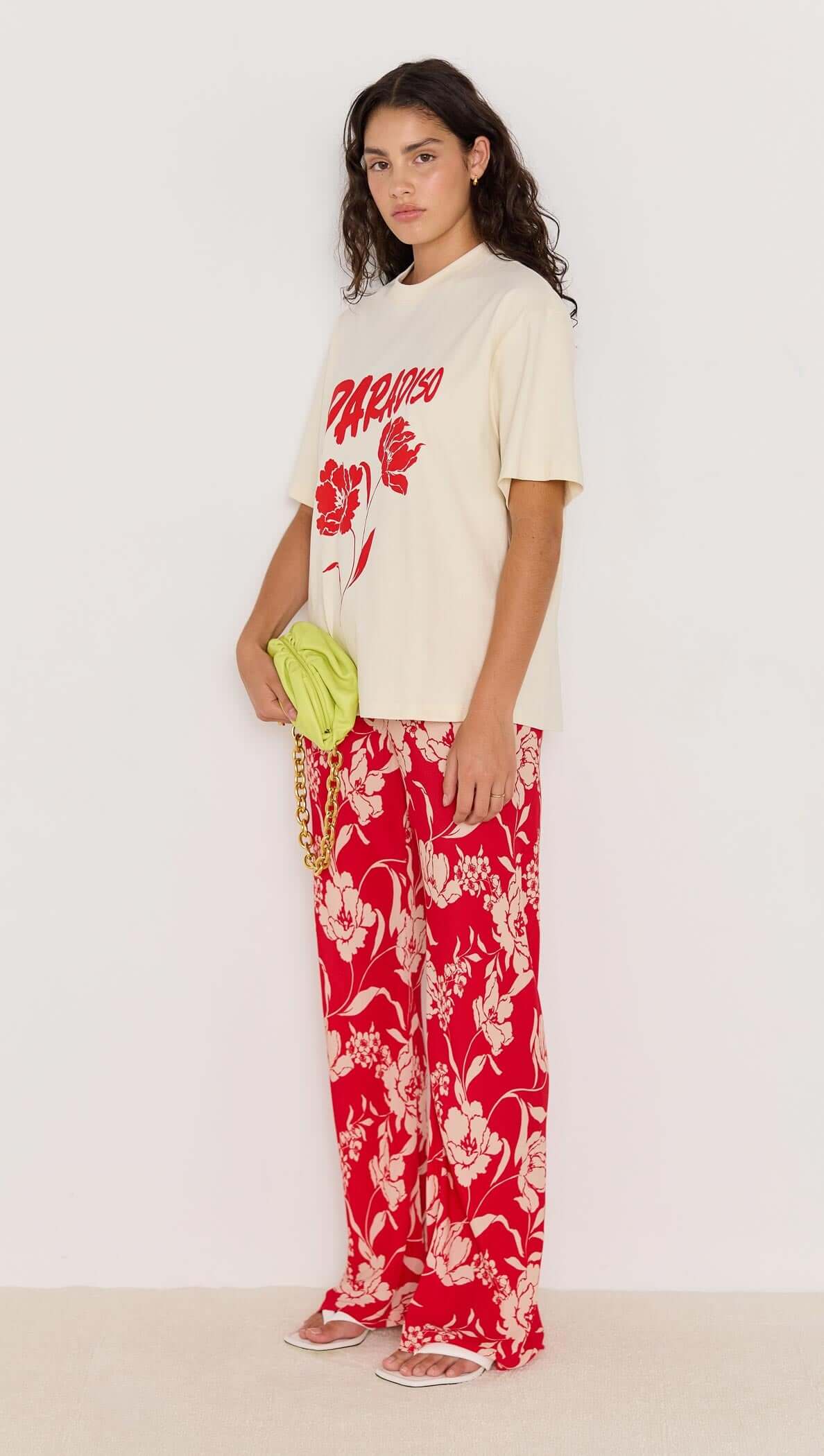 Model wearing relaxed-fit beige t-shirt and red floral Poppy Pants with wide legs, showcasing summer style.
