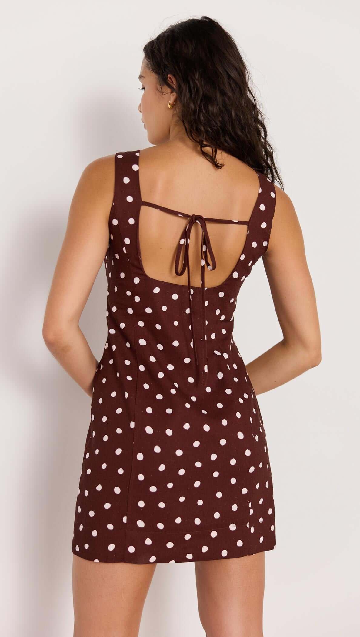 Back view of the Cedar Spot Mini Dress in chocolate brown with white polka dots and tie closure.