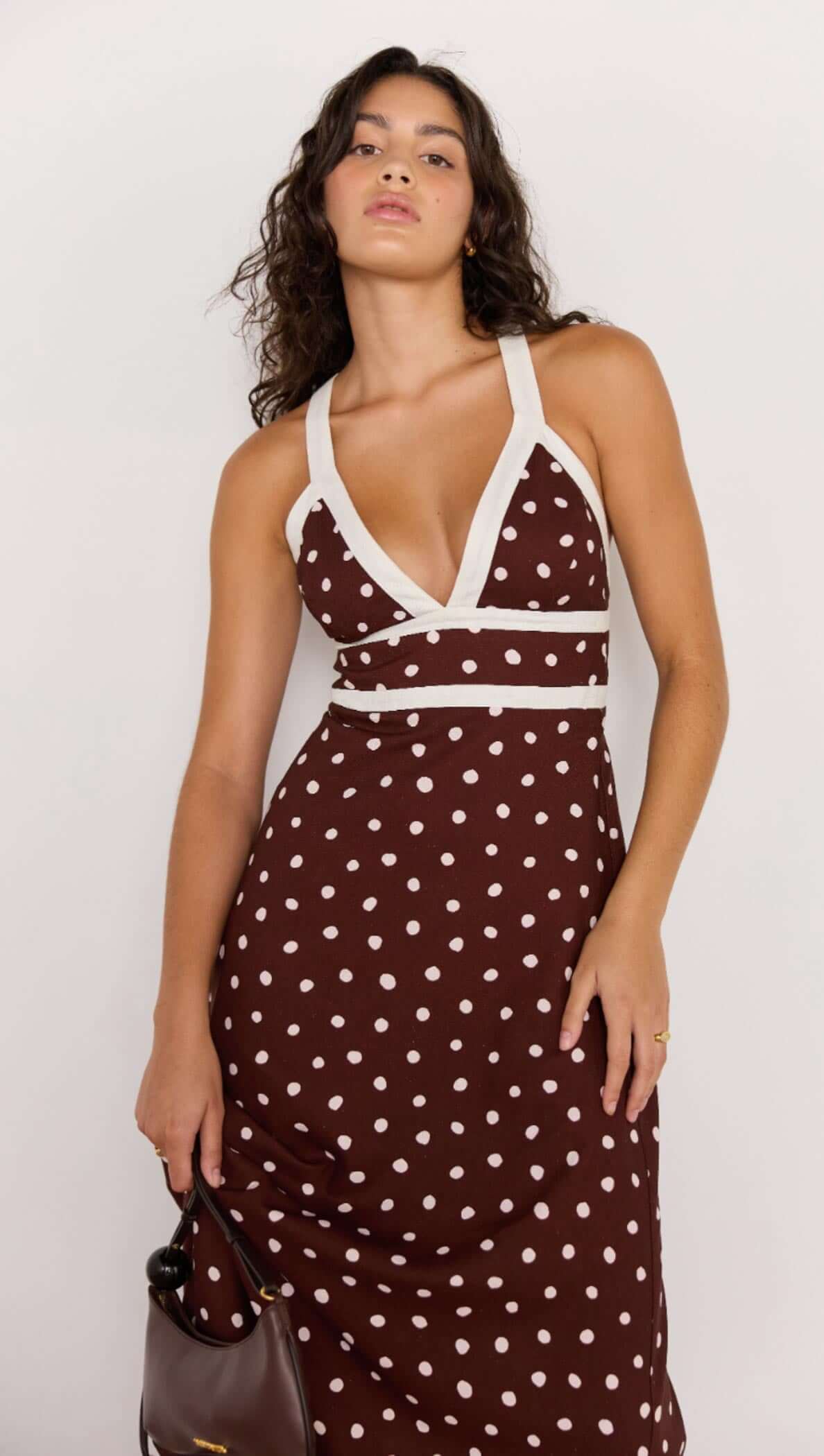 Model wearing the Cedar Spot Cross Back Dress in chocolate brown with white polka dots and contrasting trim.