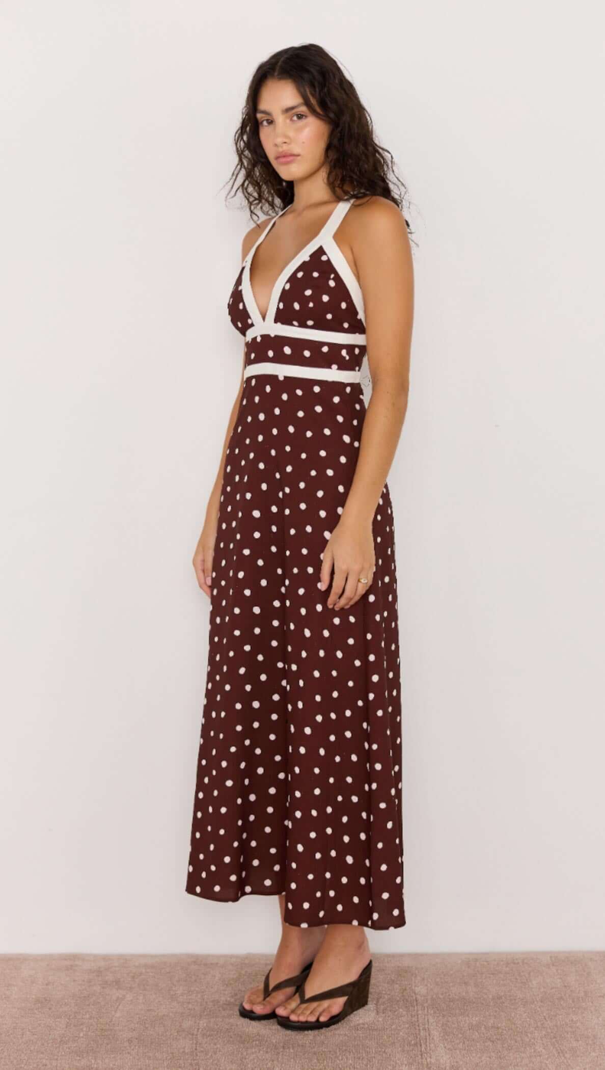 Model wearing a chocolate brown polka dot midi dress with a deep V-neckline and cross-back straps.