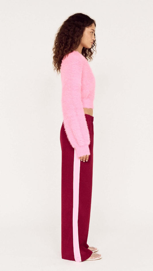Side view of a model wearing the Clio Cropped Fuchsia Pink Fluffy Jumper with burgundy pants featuring a pink stripe.