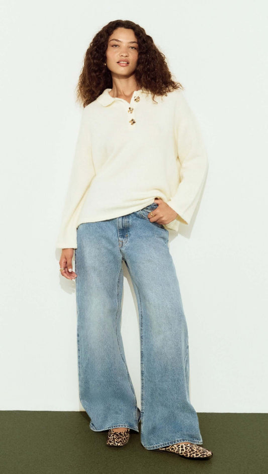 Woman wearing a Gold Detail Relaxed Polo Knit with wide-leg jeans and stylish shoes, showcasing a relaxed and fashionable look.