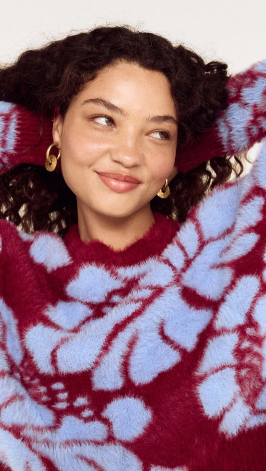 Model wearing an Intarsia Floral Soft Touch Jumper with a playful floral design in red and blue.