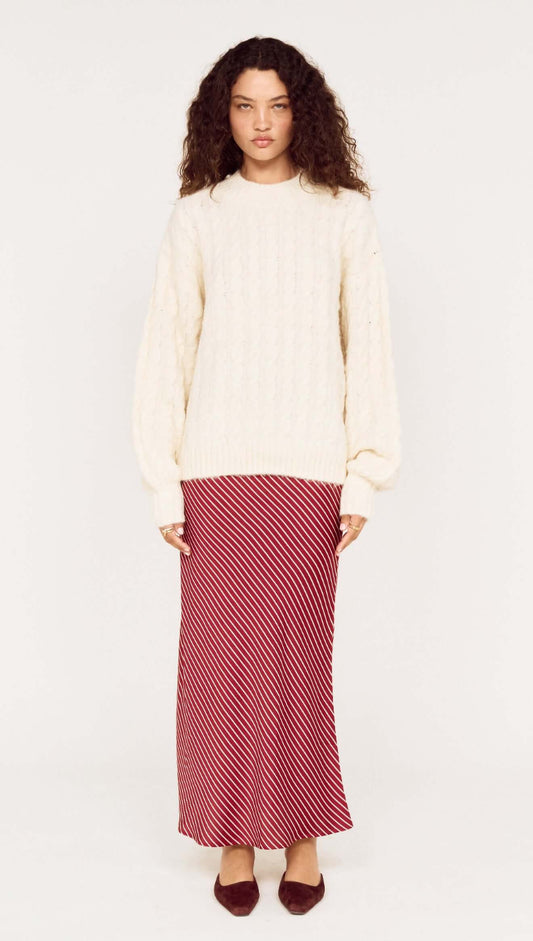 Model wearing a beige knit sweater with a Burgundy Pinstripe Bias Midi Skirt and brown shoes.