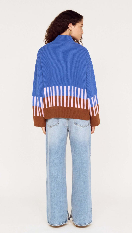 Back view of a woman wearing a cobalt blue intarsia detail jumper with brown and light purple stripes.