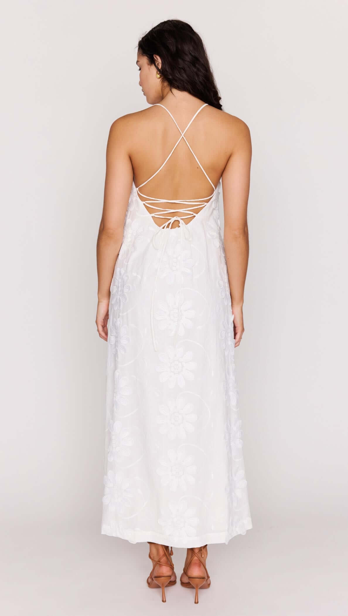 Back view of a woman wearing a White Cotton Floral Applique Lace-Back Maxi Dress showcasing the intricate lace-up detail.