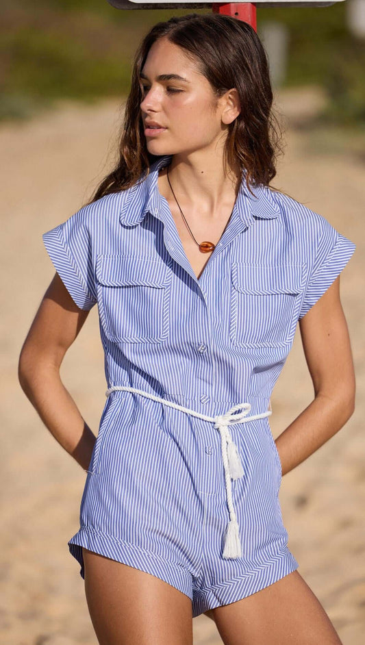 A woman wearing a Blue & White Stripe Playsuit on the beach, featuring a button-down front and elastic waist.