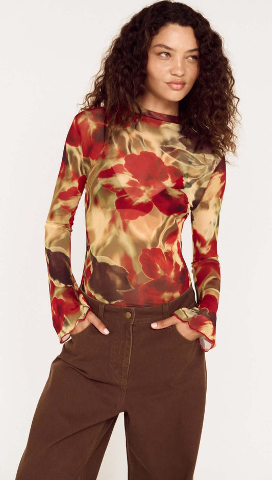 Model wearing a Red Floral Sheer Mesh High Neck Top with bell sleeves and brown pants.