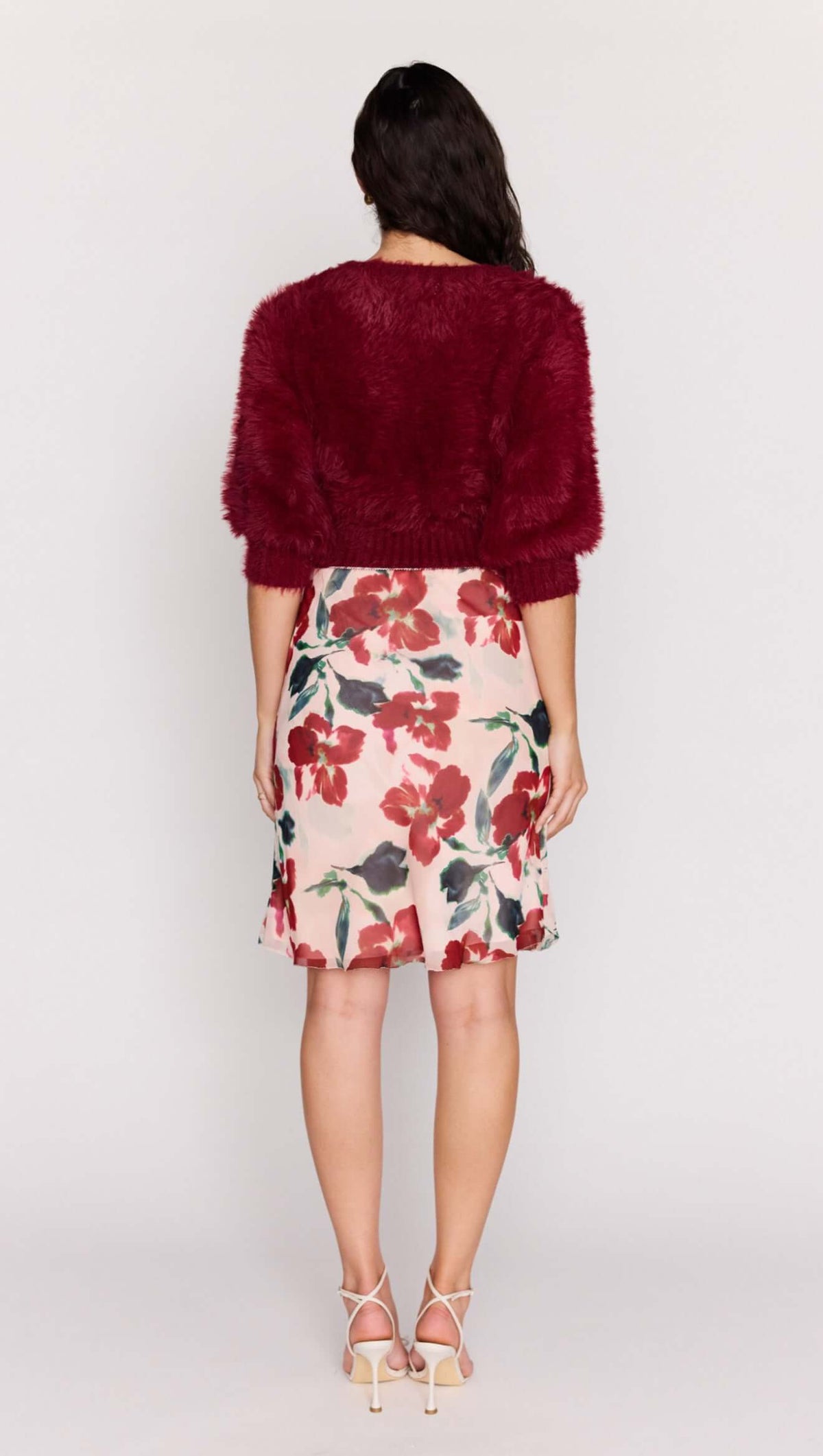 A model wearing a Burgundy Cropped Fluffy Knit Sweater paired with a floral skirt from the back.