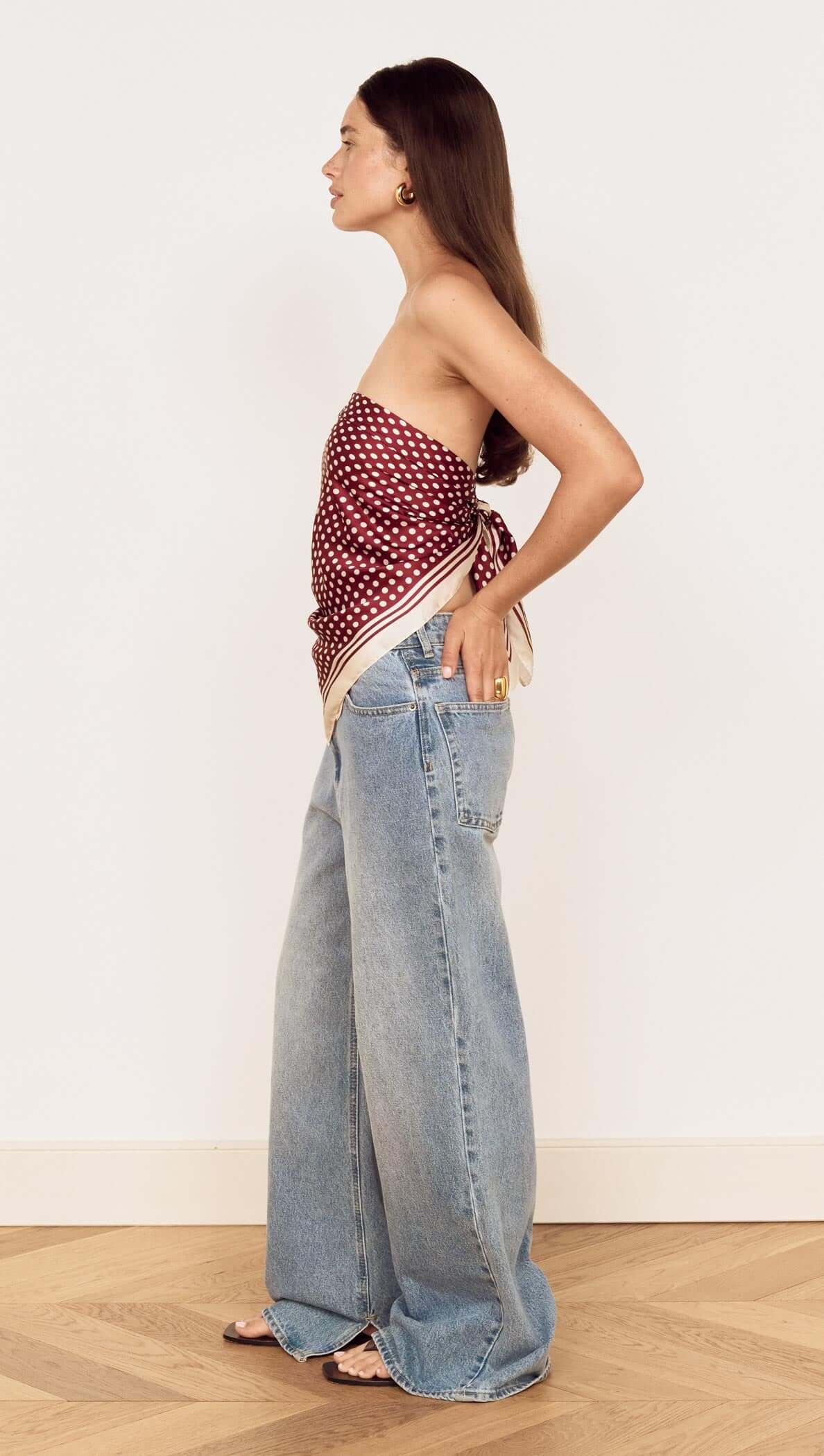 Model showcasing the Chocolate Polka Dot Scarf styled as a bandeau top with high-waisted denim jeans.
