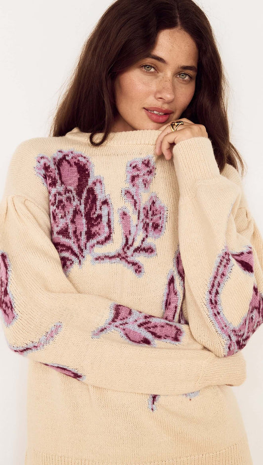 Model wearing a Cream Floral Intarsia Knit Sweater with floral motifs in wine and lilac, smiling at the camera.