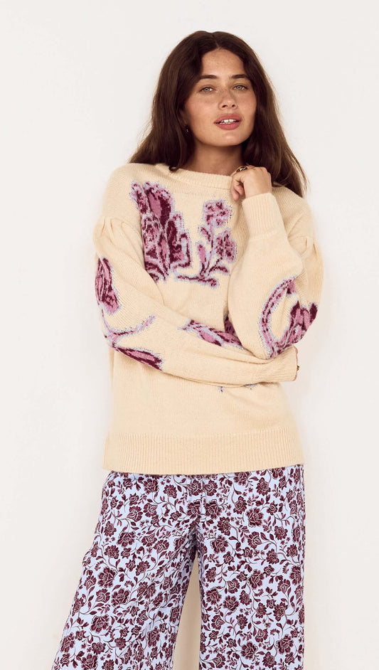 Woman wearing a Cream Floral Intarsia Knit Sweater featuring floral motifs in wine and lilac, styled with printed trousers.