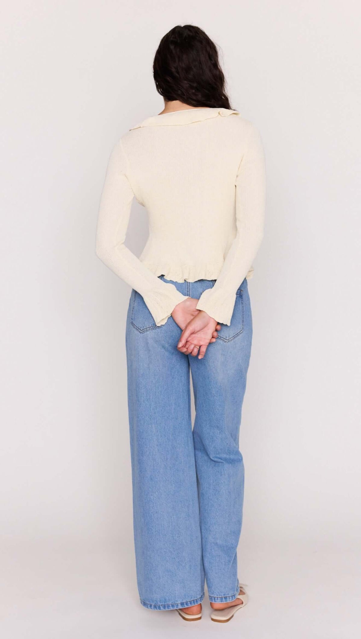 Back view of a model wearing a Cream Ruffled Cardigan with fluted hems and casual blue jeans.