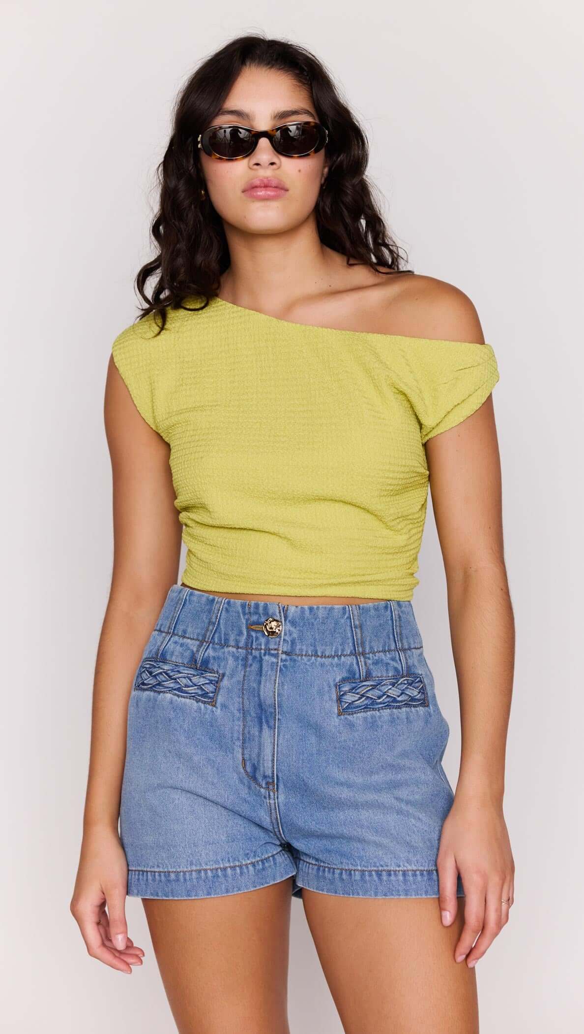 Model wearing High Waisted Cotton Blend Denim Short paired with a yellow cropped top and sunglasses.