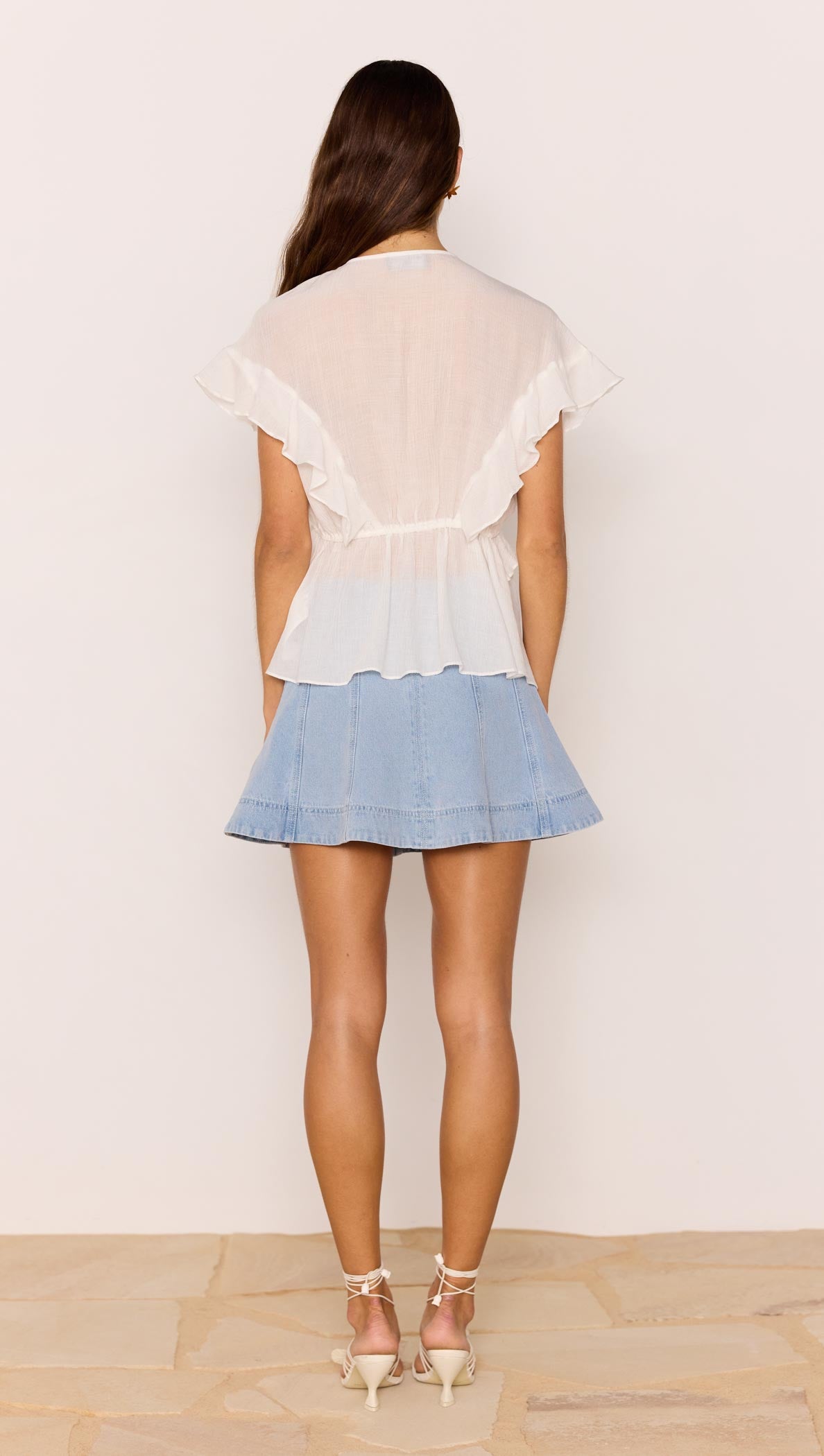 Back view of the Marlon White Ruffle Blouse styled with a denim skirt, showcasing flutter sleeves and ruffle detailing.