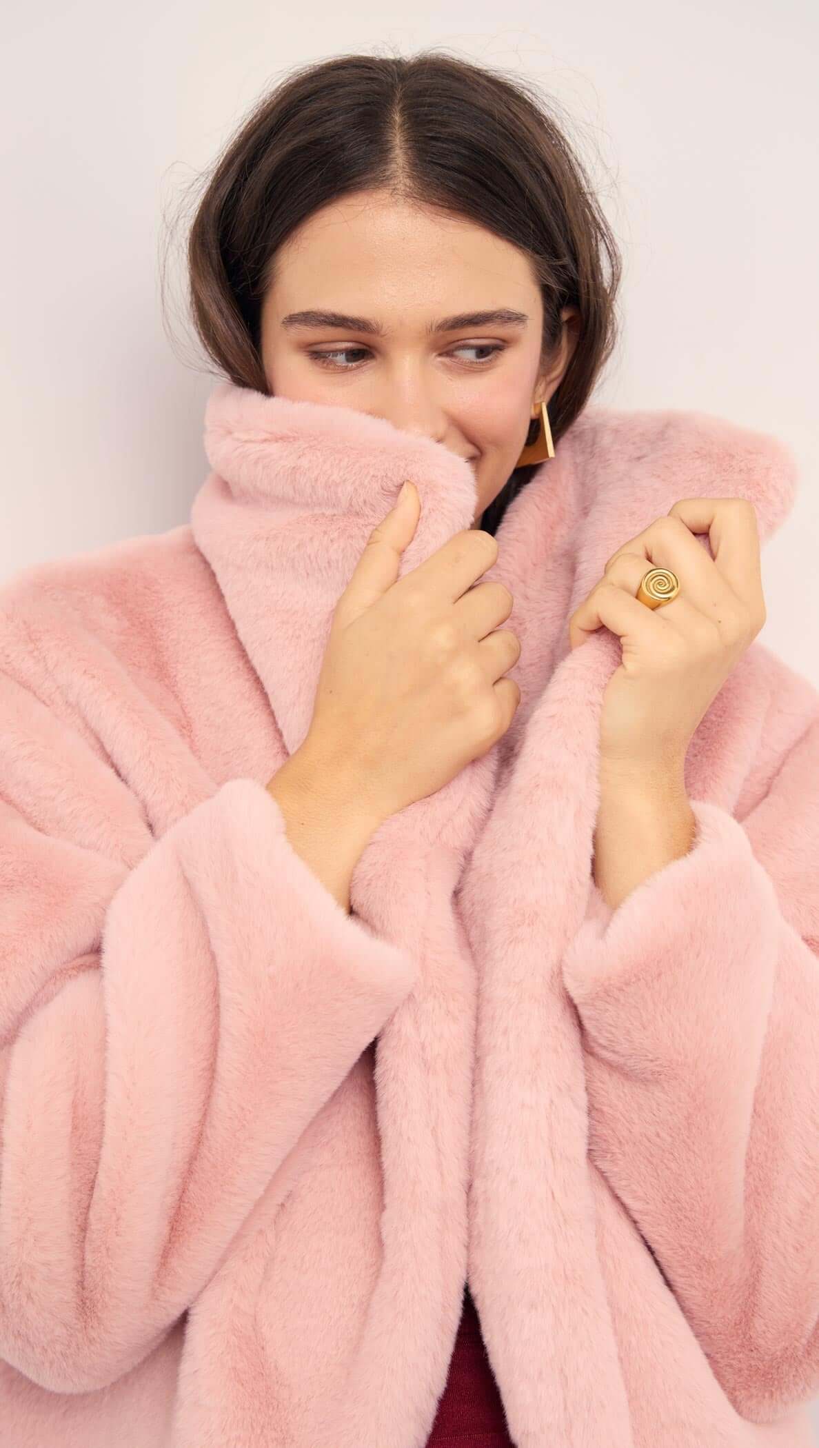 Woman wearing a Dusty Pink Faux Fur Coat, smiling and wrapping herself in the plush fabric for warmth.