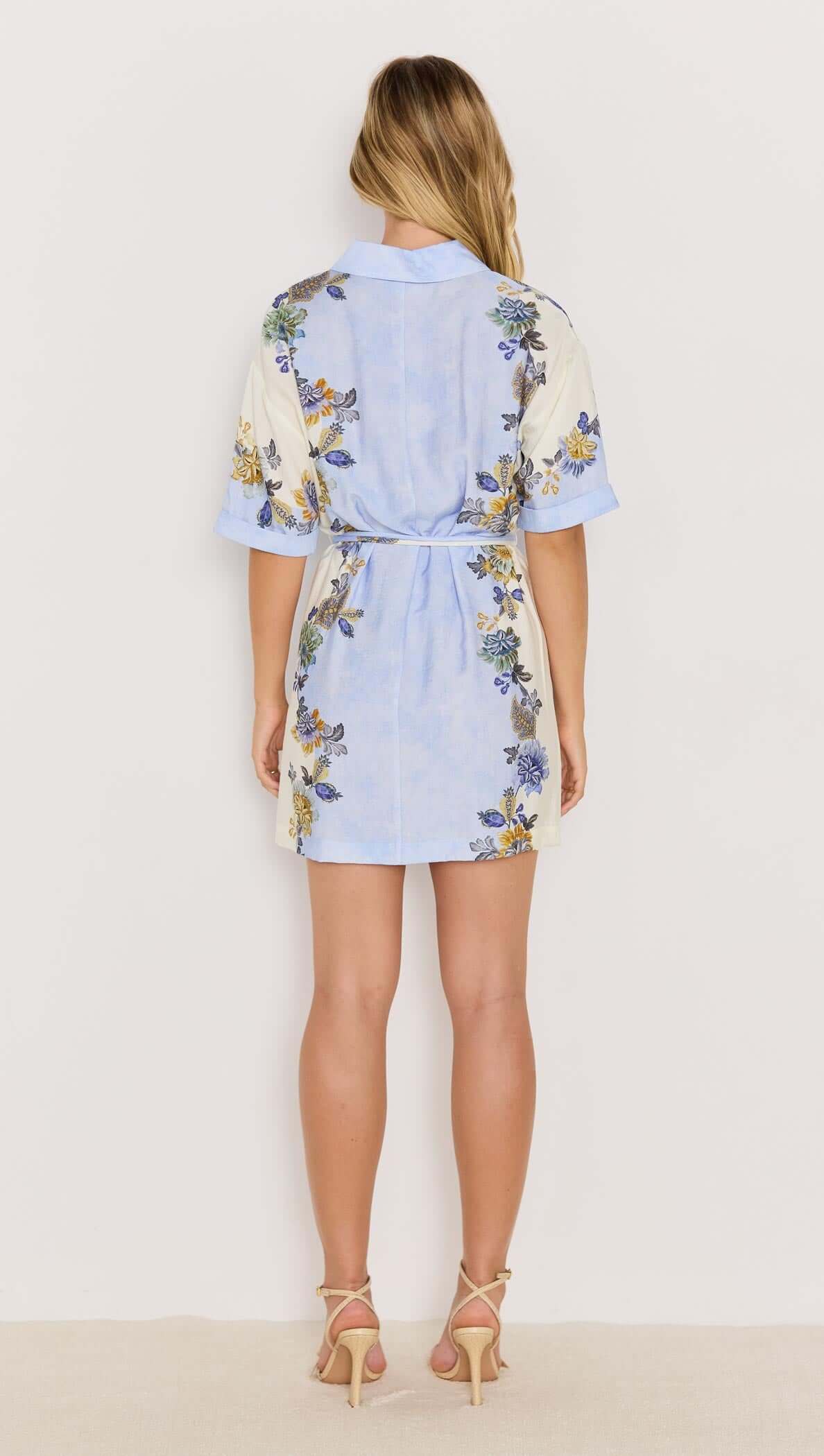 Back view of the Lucia blue floral mini shirtdress with tie waist, showcasing vibrant floral prints and rolled short sleeves.