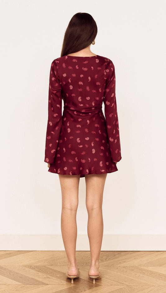 A woman wearing the Wine Satin Paisley Knot Front Bias Mini Dress, showcasing the back view with long flared sleeves.