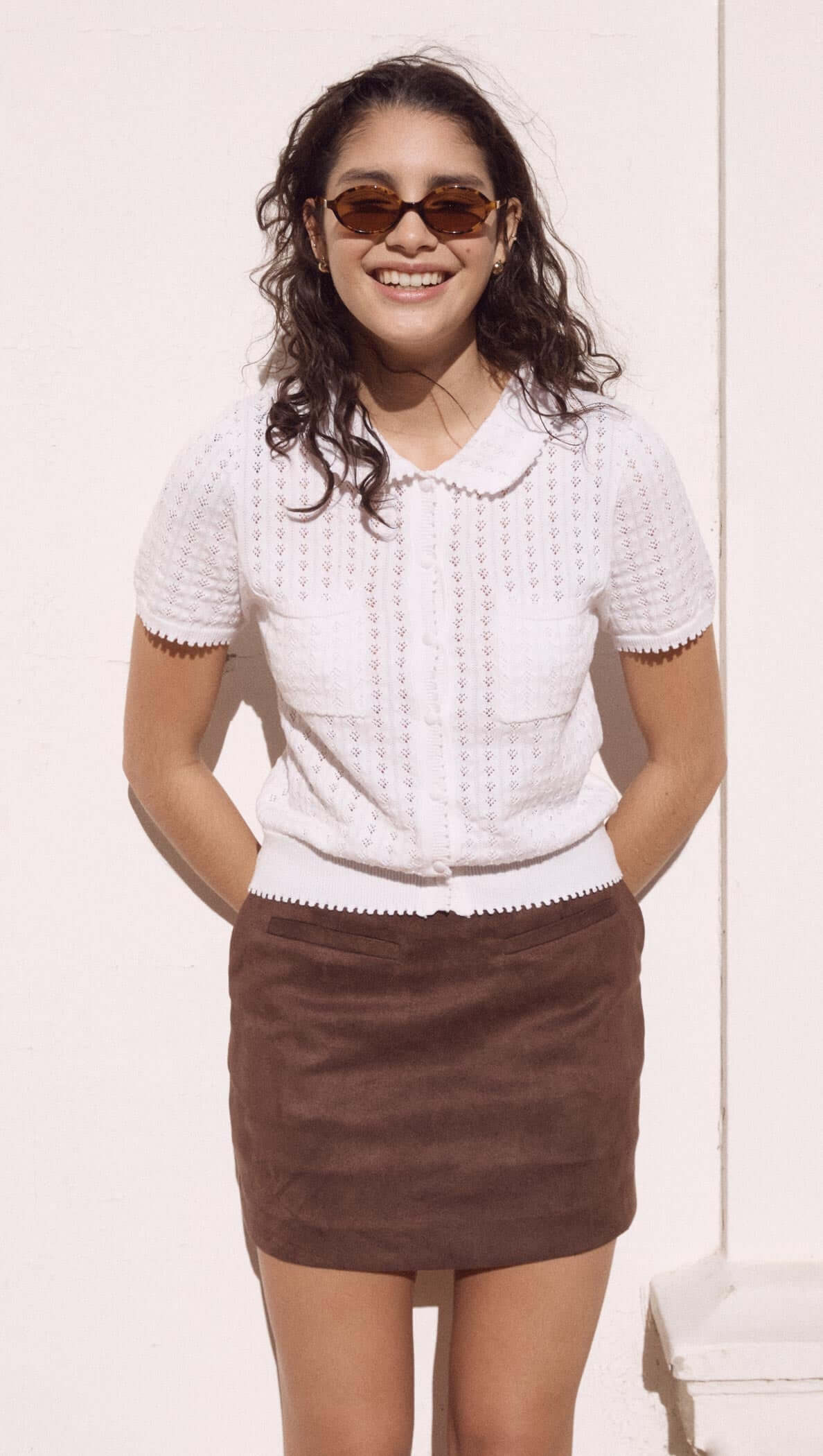 Model wearing a French Pointelle short sleeve knit top in white with a collar, paired with a brown skirt and stylish sunglasses.