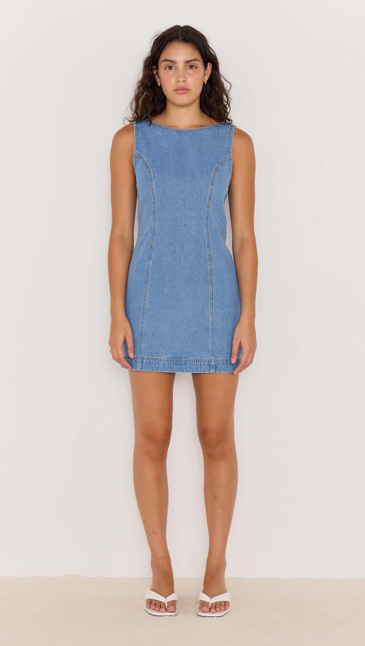Model wearing a blue denim scoop back mini dress with a fitted silhouette and clean lines.