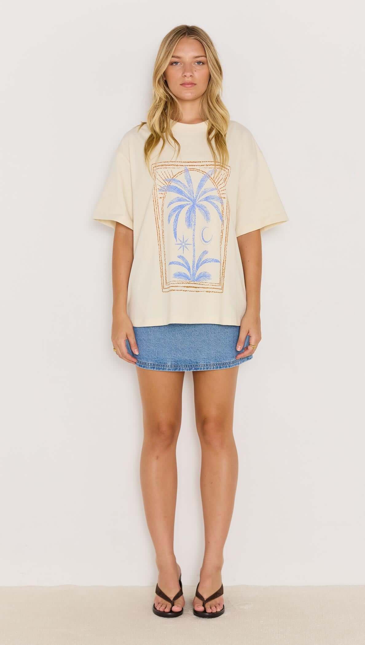 Model wearing a Palm Print Cotton Oversize T-Shirt styled with a denim skirt and sandals, showcasing a relaxed coastal vibe.