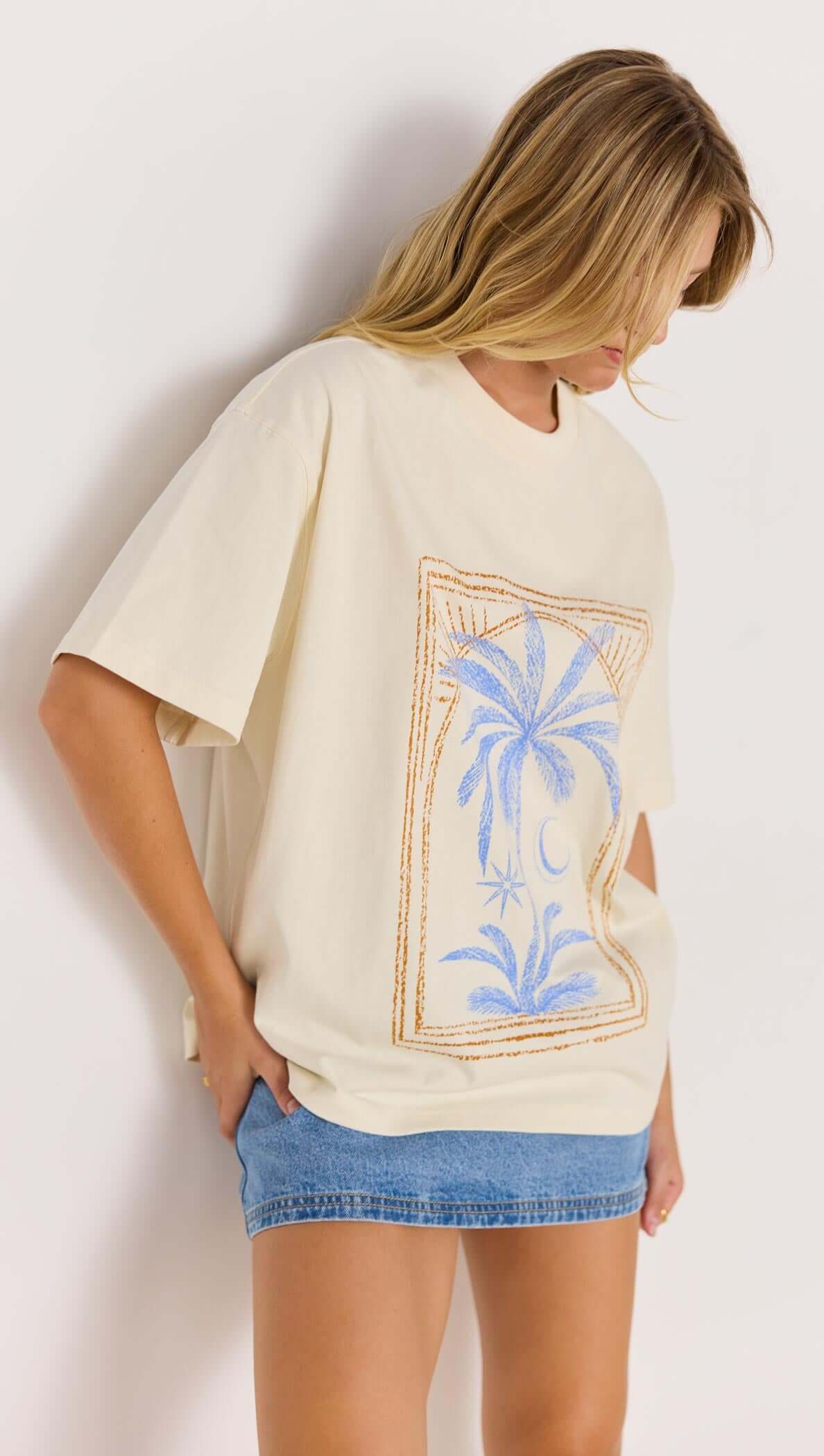 Palm print cotton oversize t-shirt in cream color, styled with denim shorts, showcasing a coastal aesthetic.