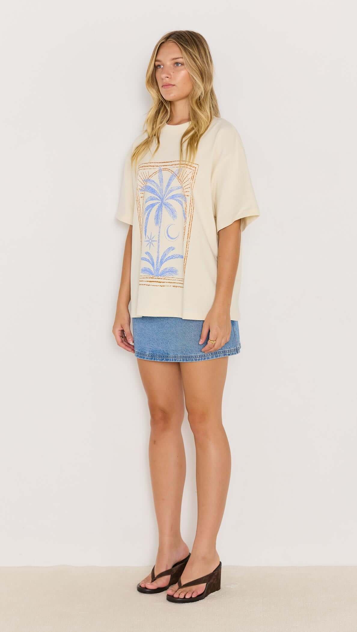 Model wearing a palm print cotton oversize t-shirt paired with a denim mini skirt and sandals, ideal for a casual summer look.