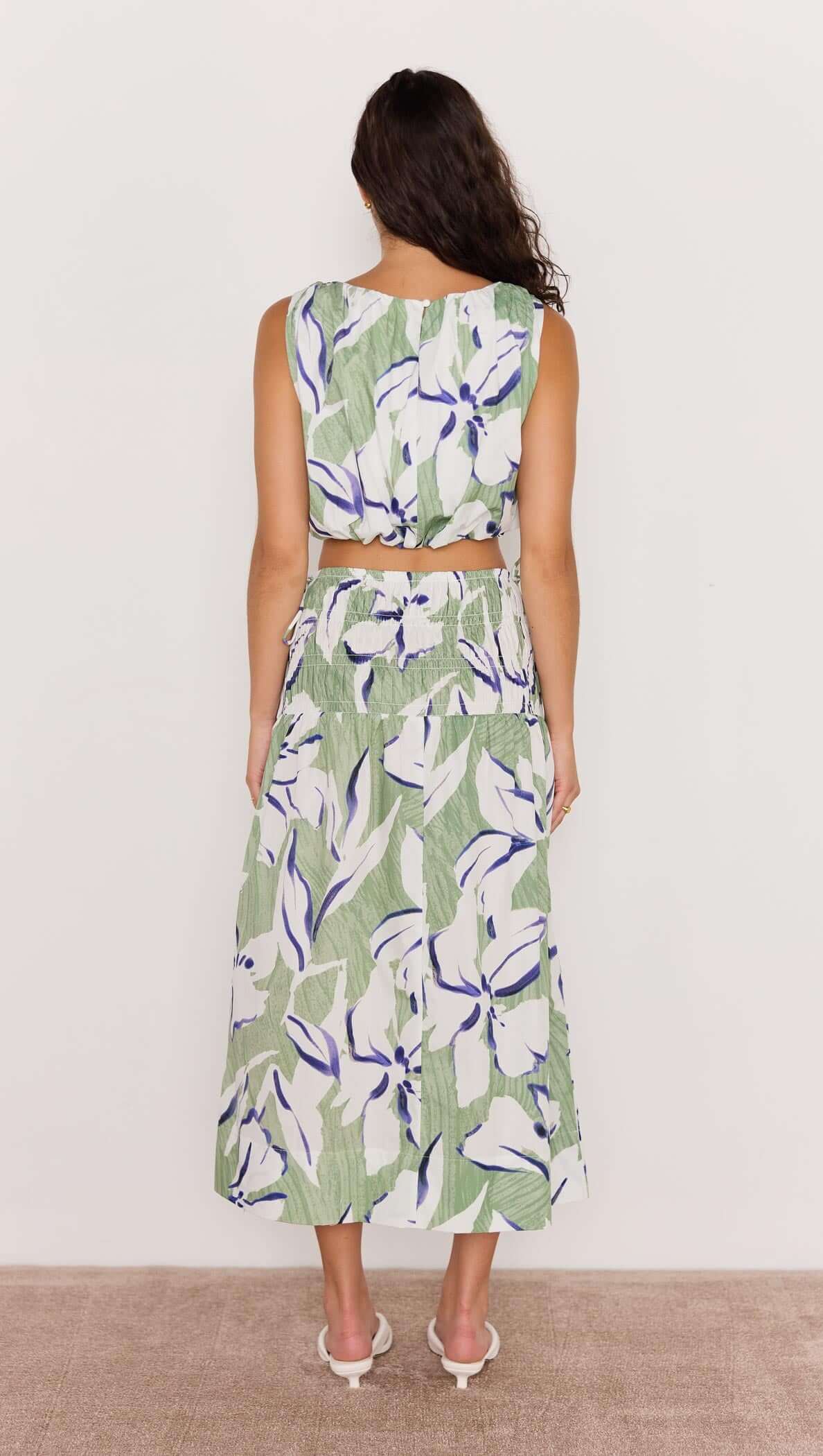 Back view of a model wearing a green and white floral midi skirt paired with a matching crop top, showcasing a breezy summer style.