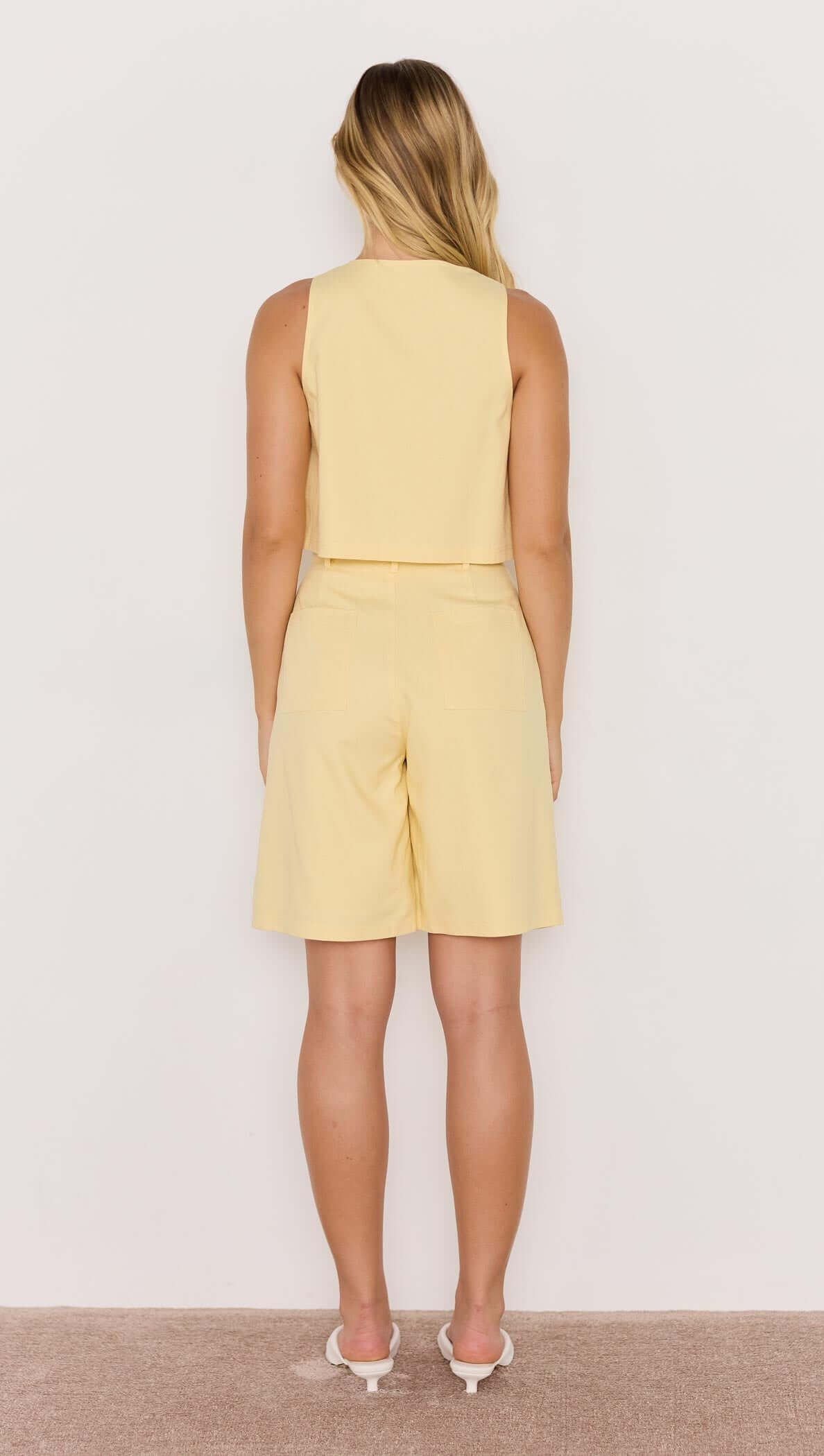 Back view of a model wearing a butter yellow crop top with matching shorts, showcasing a casual summer outfit.