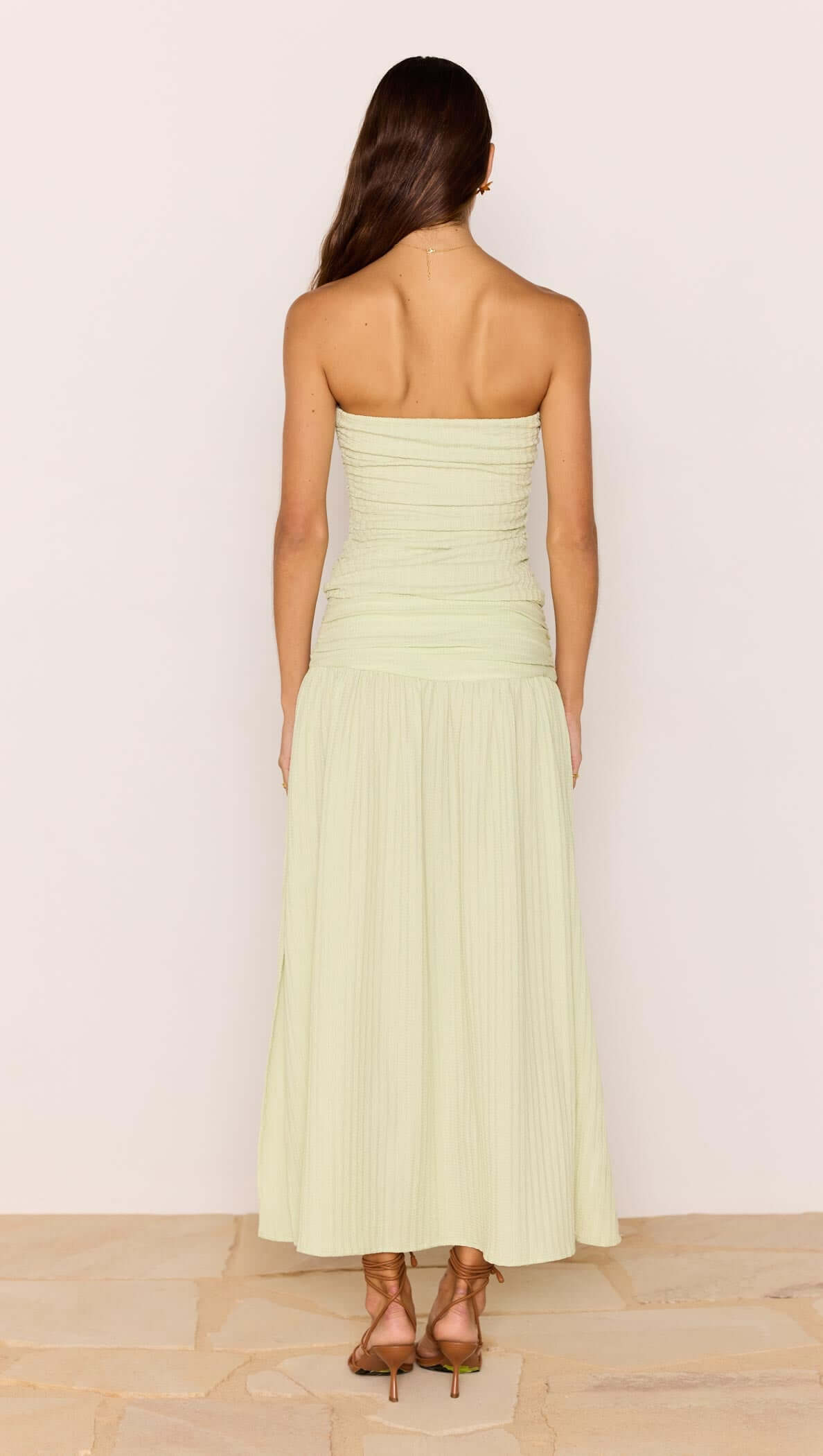 Back view of a woman wearing a Chloe Pistachio Side Split Maxi Skirt with a strapless top in soft green.