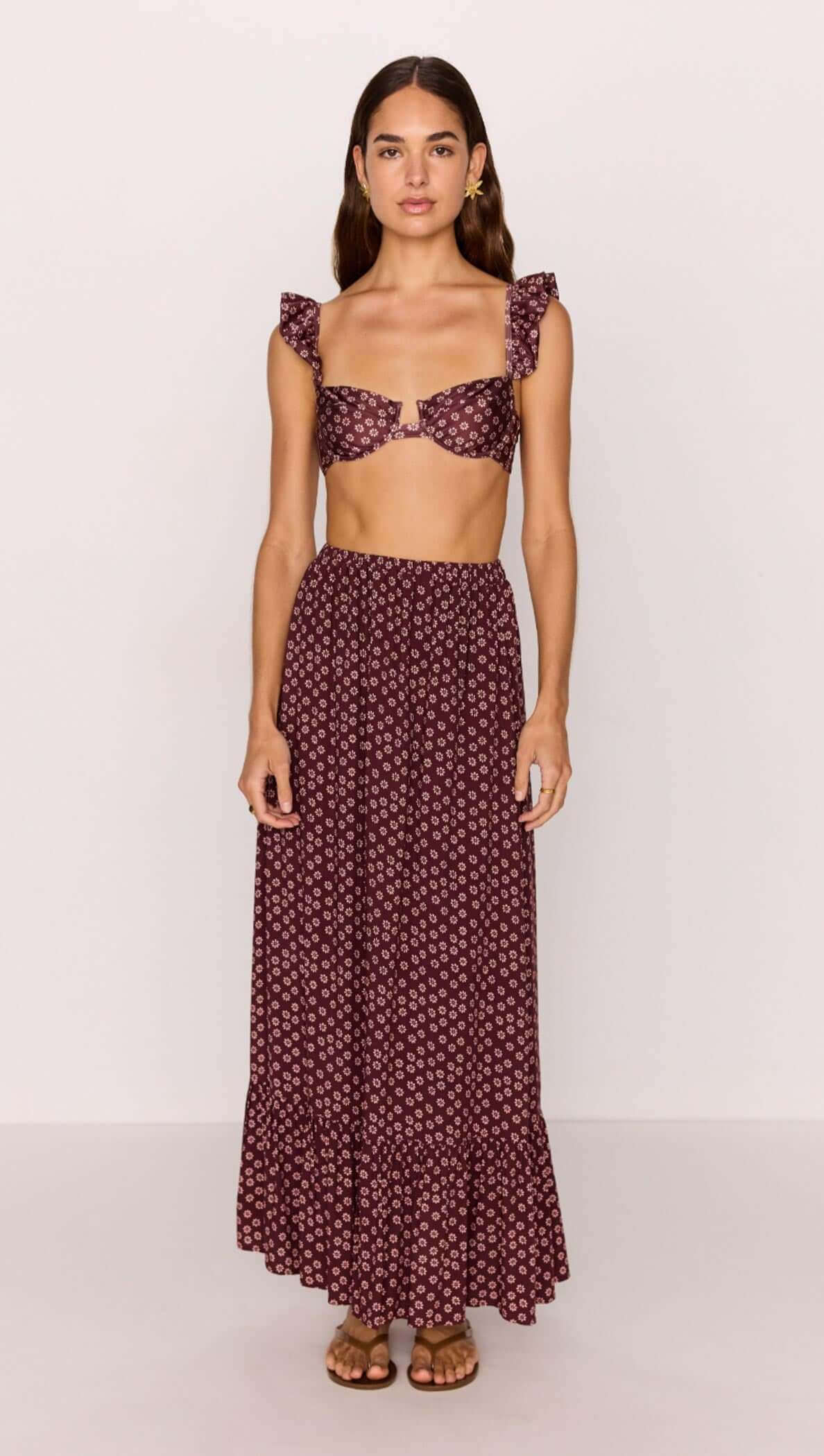 Woman wearing a burgundy floral print ruffle hem maxi skirt with matching crop top.