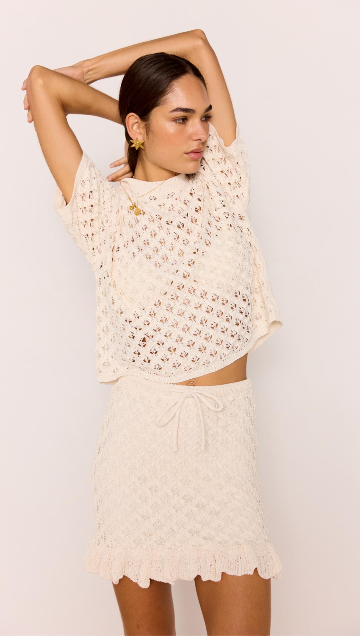 Woman wearing a White Pointelle Knit Mini Skirt with matching top, showcasing a cream open-knit design and ruffled hem.