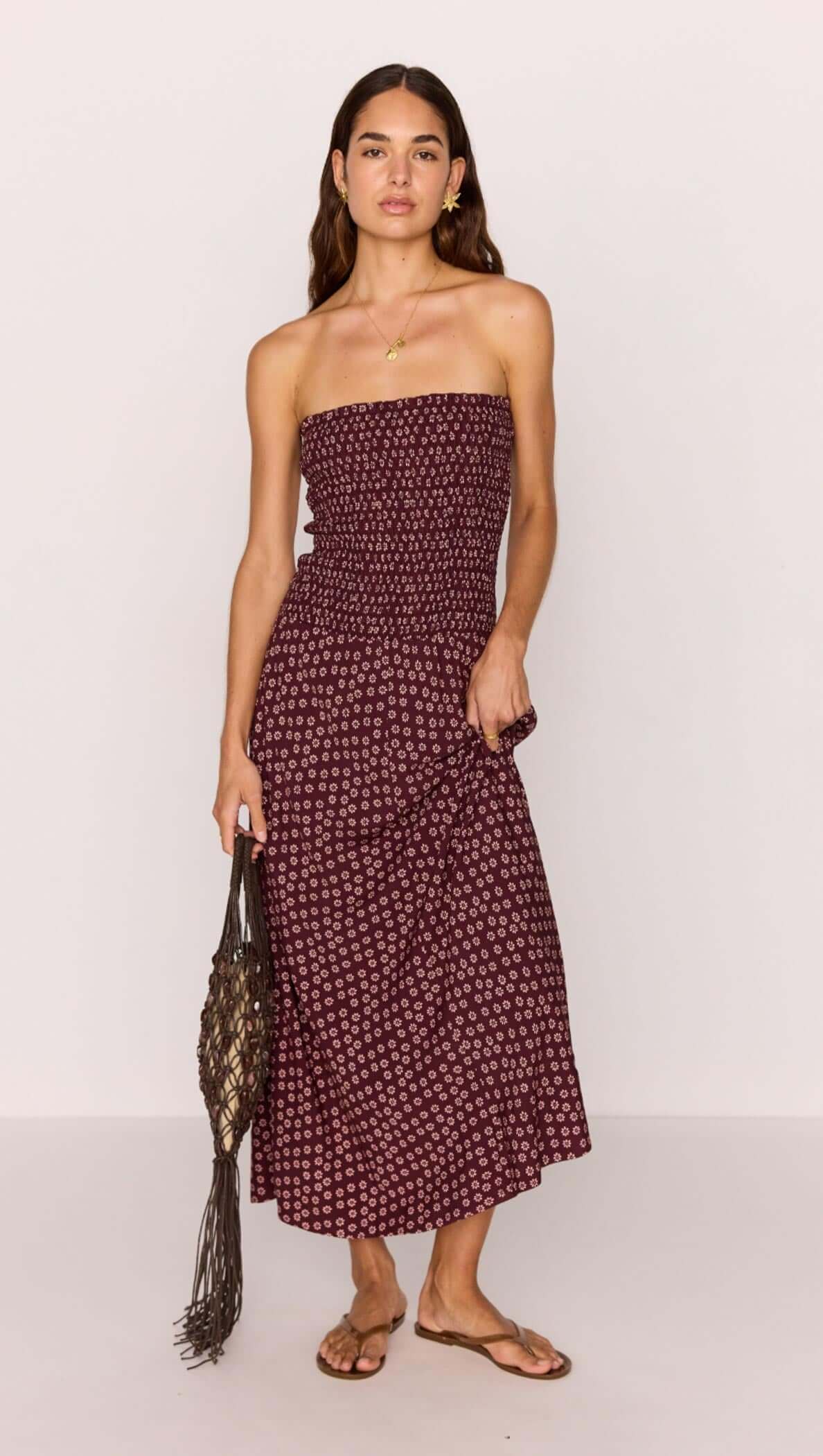 Model wearing a strapless burgundy floral print maxi dress with a ruched bodice and dropped hem, holding a handbag.