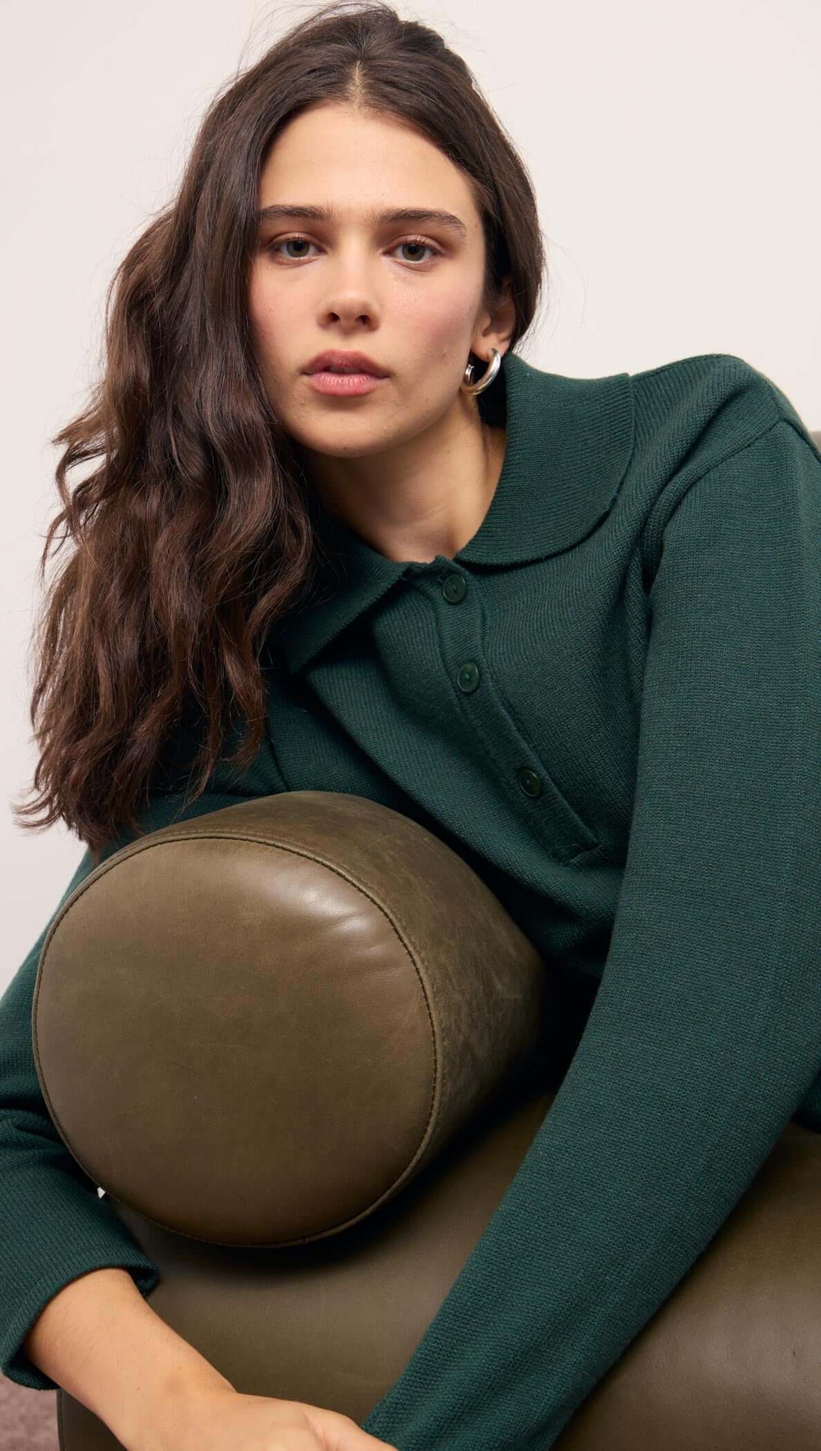 Model showcasing the Teal Green Knit Polo Sweater with a structured collar, relaxing on a green sofa.