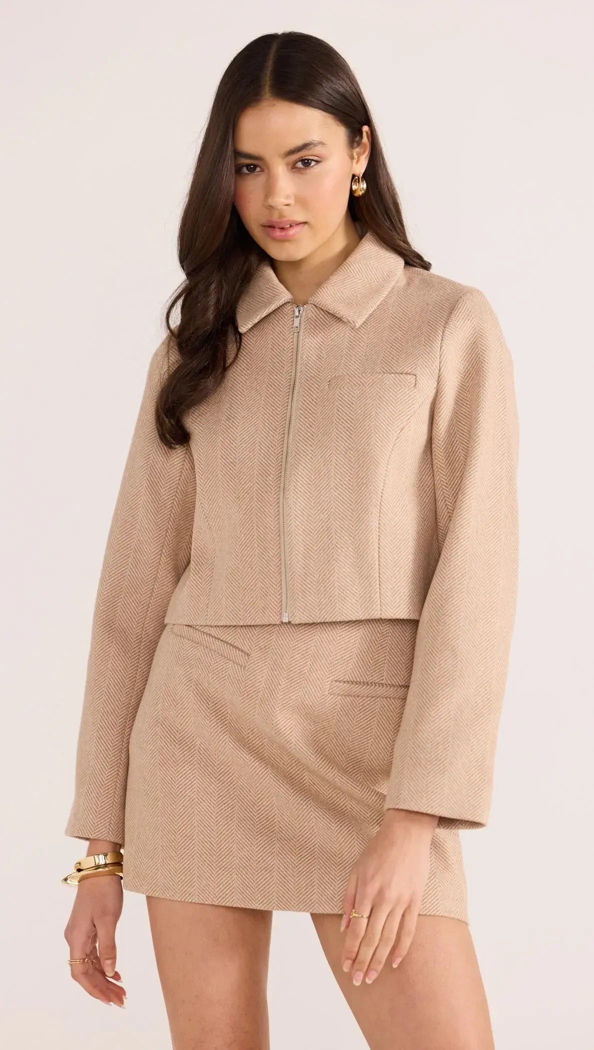 Model wearing a beige Audrey Herringbone mini skirt and matching jacket, showcasing a stylish high-rise fit and tailored lines.