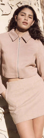 Model wearing a cropped beige jacket and matching mini skirt, showcasing a stylish brown herringbone pattern.