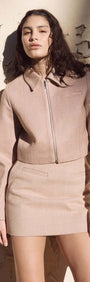 Model wearing Audrey Herringbone Mini Skirt and matching jacket against a textured wall, showcasing modern classic style.