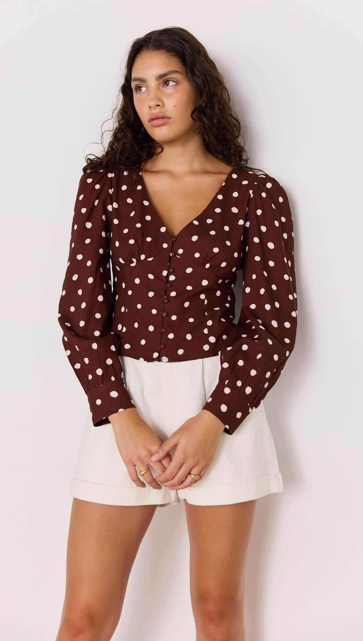 Model wearing the Cedar Spot Corset Blouse in chocolate brown with cream spots and puffed sleeves.