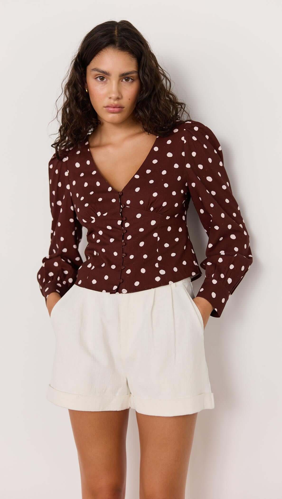 Flattering chocolate brown corset blouse with cream spots, puffed sleeves, and button-up front, styled with white shorts.