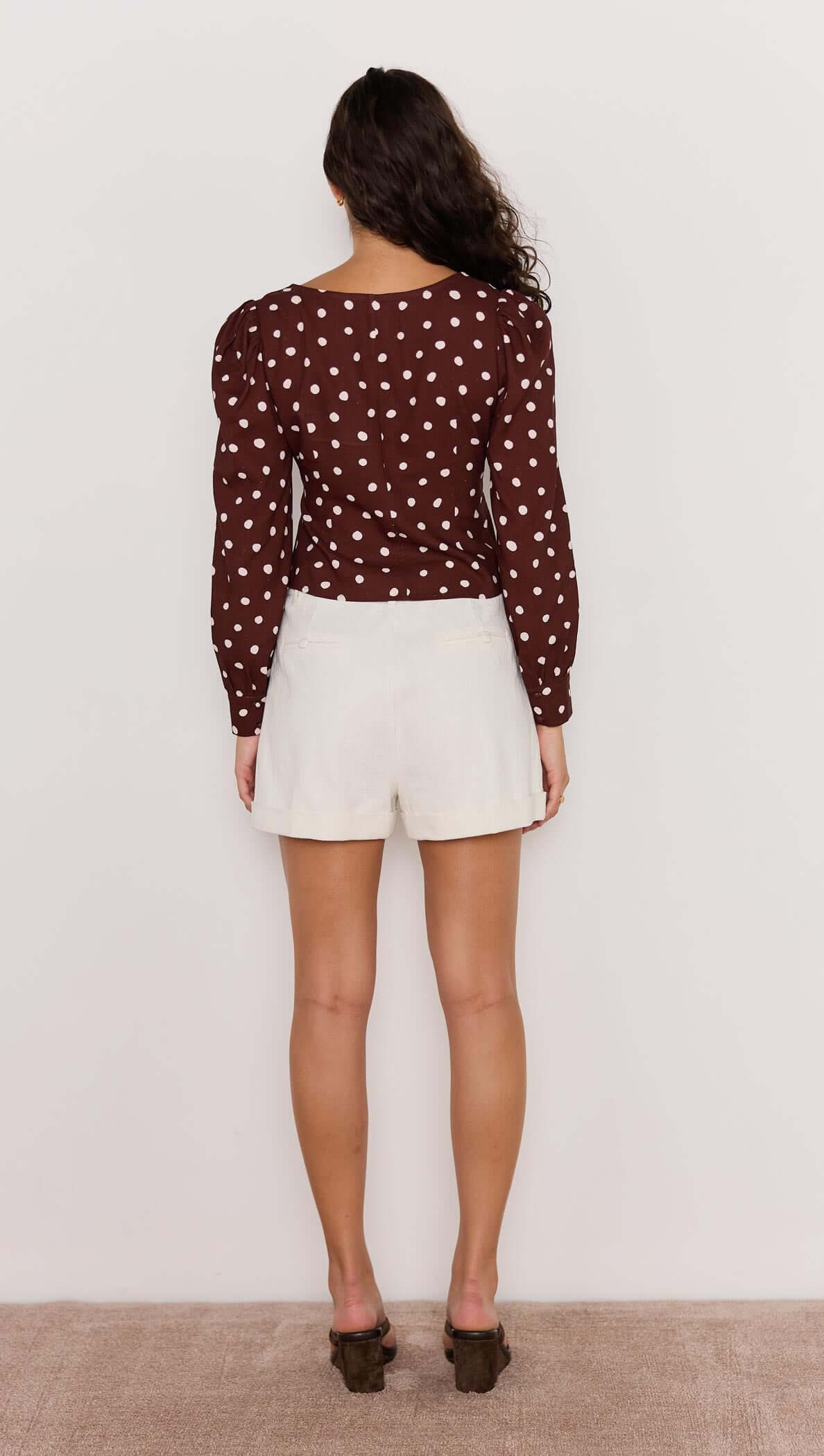 Back view of a model wearing the chocolate spot corset blouse with puffed sleeves and white shorts.